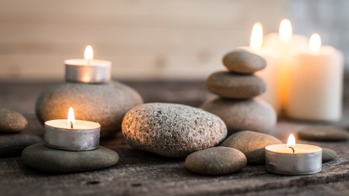 Collection of smooth grey stones, some stacked, atop a gray wooden surface surrounded by soft, lit tea light and pillar candles, providing a sense of calm and relaxation that I tried to create on my dilator journey.