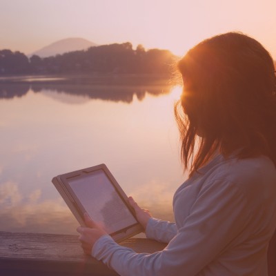 Person reading a tablet outside near a lake at sunset reading a blog from The Lost labia Chronicles on their ipad.