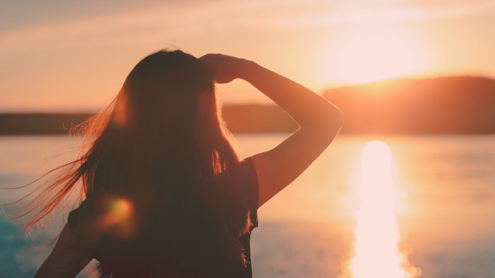 Image of a person from behind, looking into the horizon of a sunset on a still body of water.