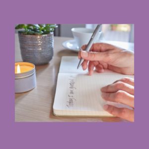 Image of a desk with a succulent, a candle, and a person writing in a gratitude journal. The background is a pale purple.