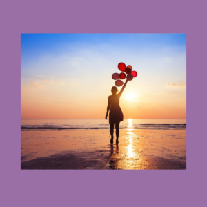 Image of a person standing on a sunny, shallow area of an ocean holding a bunch of red balloons over their head.