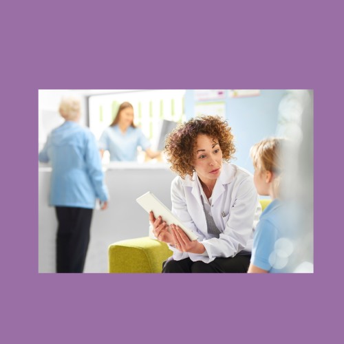 Image of a doctor in a white labcoat with short, curly hair, talking to a patient, who can can see from behind with blonde hair and a blue shirt. This represents me getting my lichen sclerosus diagnosis.