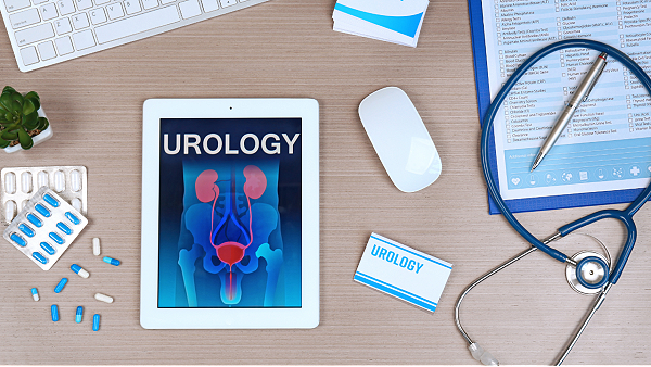 Image of a desk with office supplies on it. In the center is a white tablet with the word 'urology' in white, capital letters, with a black background and an anatomical model of the pelvis.