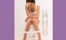 Image of a person with pale skin in a white shirt sitting on a white toilet with white underwear between their legs.