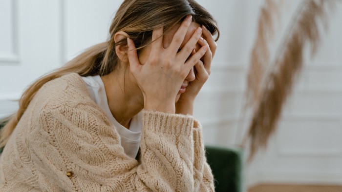 Image of a white person with a big beige sweater sitting down with their hands over their head in expression of hopelessness, fear, anger, and grief.